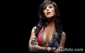 Фотография Kat Von D с ярким макияжем и татуировками на руках и теле, на черном фоне.