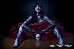 Фотография Kat Von D в черном платье и перчатках, держащей череп, с татуировками на руках и теле.
