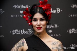 Фотография Kat Von D с ярким макияжем и татуировками на руках и шее, на фоне черного баннера с логотипом Kat Von D Beauty.