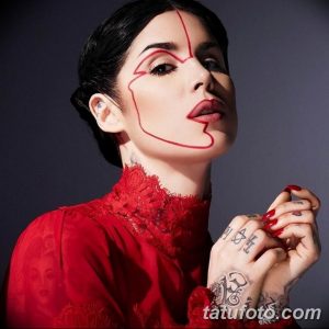 Фотография Кат фон Ди с татуировками на руках и лице, а также с необычным макияжем в виде красных линий на лице. Стильный и креативный образ.
