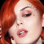 Фотография девушки с рыжими волосами и татуировками в виде звезд на лице, демонстрирующая яркий макияж.