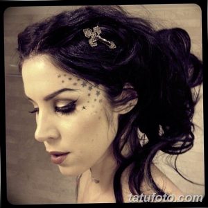 Фото Kat Von D: тату-мастер с татуировками в виде звезд на лице и татуировками на шее. Детальный портрет с акцентом на татуировки.