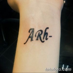 Фото тату: маленькая черная надпись 'ARh-' на запястье. Простой и лаконичный рисунок татуировки, выполненный четкими линиями.