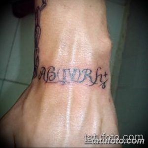 Фото татуировки на запястье с надписью 'AB Rh+', выполненной каллиграфическим шрифтом черными чернилами.