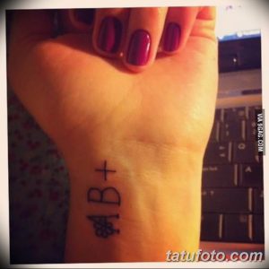 Фото татуировки на запястье с надписью 'AB+' и изображением капли крови, выполненной черными чернилами.