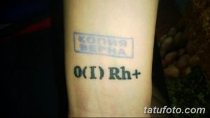 Фото тату группы крови 'O(I) Rh+' и символа в виде квадрата с надписью на руке. Небольшой, простой рисунок татуировки, выполненный в черном цвете.