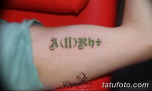 Фото тату группы крови 'A(II)Rh+' на внутренней стороне предплечья. Небольшой, аккуратный рисунок татуировки, выполненный в зеленоватых тонах.