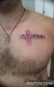 Фото тату: готическая надпись 'A(II)Rh+' с красными брызгами на груди. Рисунок татуировки выполнен в черном и красном цветах.