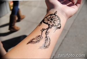 Фото татуировки ловца снов на запястье. Детализированный рисунок с перьями и бусинами, выполненный черными чернилами.