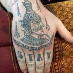 Фото тату на руке с изображением портрета в традиционном стиле и надписью STAY. Детализированный рисунок с использованием черных и серых оттенков.