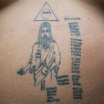 Фото тату: изображение Иисуса Христа с нимбом и текстом на спине человека, выполненное в простом, схематичном стиле.