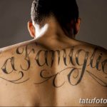 Фото тату на спине с надписью 'La Famiglia' выполненной красивым шрифтом. Черно-белая татуировка.