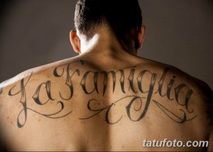 Фото тату на спине с надписью 'La Famiglia' выполненной красивым шрифтом. Черно-белая татуировка.