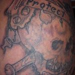 Фото тату: черно-серый череп с надписью 'Protect' и лентой с текстом 'Family'. Рисунок выполнен в стиле олдскул на плече.