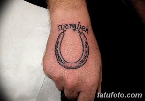 Фото татуировки на руке: изображение подковы с надписью "marchek". Простой и минималистичный рисунок.