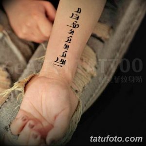 Фото тату с иероглифами, расположенными вертикально на запястье, выполнено в черном цвете.