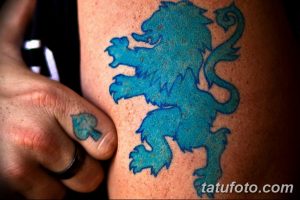 Фото татуировки на руке с изображением голубого льва, смотрящего вправо, и маленькой татуировки на пальце.