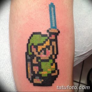 Фото тату пиксельного Линка с мечом из The Legend of Zelda на руке. Яркий и динамичный рисунок в стиле 8-bit, выполненный в зеленых и синих тонах.