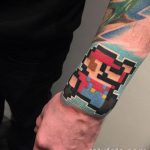 Фото татуировки в стиле пиксель-арт с изображением Марио из игры Super Mario Bros. на руке. Яркие цвета и четкие линии.