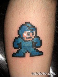 Фото тату с изображением пиксельного Мегамена из игры Mega Man на ноге. Синий персонаж в динамичной позе.
