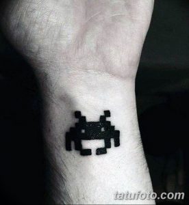 Фото тату с изображением пиксельного инопланетянина из игры Space Invaders на запястье. Черный рисунок на светлой коже.