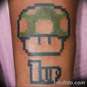 Фото тату с изображением пиксельного гриба из игры Super Mario Bros на предплечье. Под грибом - пиксельный блок с надписью 'UP'.