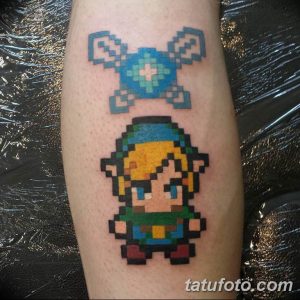 Фото тату на ноге: пиксельное изображение героя Линк из игры Zelda и символа Трифорс, выполненное в ярких цветах.