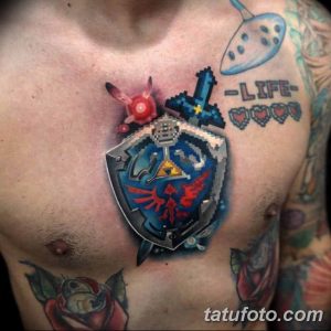 Фото татуировки на груди, изображающей пиксельный щит из игры The Legend of Zelda, окруженный другими элементами игры, выполненными в ярких цветах.