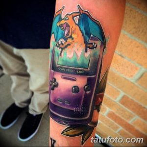 Фото тату: масштабная татуировка, изображающая Charizard из Pokemon, вылетающего из экрана Game Boy. Яркие цвета и детализированная проработка создают эффект игровой сцены на коже.