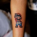 Фото тату: пиксельный Марио из игры Super Mario на предплечье. Яркие цвета и узнаваемый стиль 8-bit делают эту татуировку идеальной для поклонников ретро-игр.