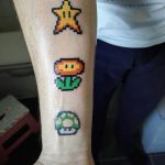 Фото татуировок в пиксельном стиле: звезда, гриб и цветок из Super Mario Bros. на руке. Яркие цвета и четкие пиксели.