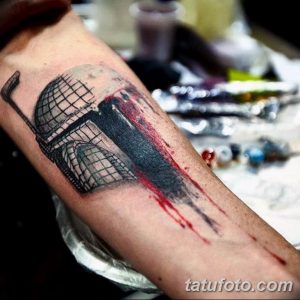 Фото тату: реалистичный рисунок шлема в стиле Star Wars с брызгами красной краски на предплечье мужчины.