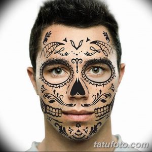 Фото тату: татуировка на лице, выполненная в стиле Day of the Dead (День мертвых). Череп украшен яркими цветами и узорами.