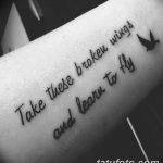 Фото татуировки на предплечье с надписью 'Take these broken wings and learn to fly' и силуэтом птицы. Черный цвет, каллиграфический стиль.
