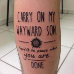 Фото татуировки на икре с текстом песни 'Carry On My Wayward Son' и символом из сериала 'Сверхъестественное'. Черный цвет, каллиграфический стиль.