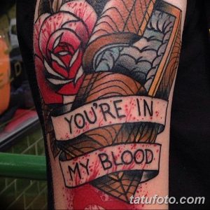 Фото татуировки на руке с изображением розы, кинжала и надписи "You're In My Blood". Яркий рисунок татуировки в стиле олдскул с использованием красного, черного и белого цветов.