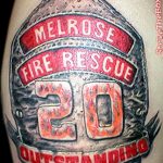 Фото тату на руке с изображением пожарного шлема с надписью 'Melrose Fire Rescue 20 Outstanding'. Детализированный рисунок татуировки.