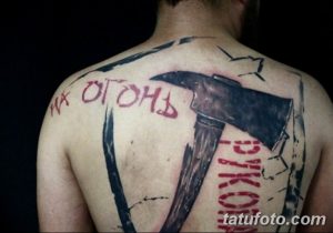 Фото тату топора с надписью на спине, выполненное в графическом стиле с использованием черного и красного цветов.