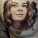 Фото тату портрета женщины с пирсингом в носу, выполненное в реалистичном стиле с использованием мягких тонов на груди.