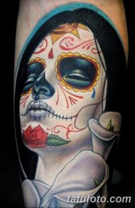 Фото тату: красочная татуировка в стиле Sugar Skull (Калавера) с изображением черепа, украшенного цветами и узорами, и красной розой на предплечье.