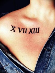 Фото тату: черные римские цифры 'X VII XIII' на женской ключице. Минималистичный дизайн, четкие линии, небольшое изображение.