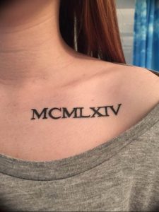 Фото тату на ключице: римские цифры 'MCMLXIV' выполнены черными чернилами, минималистичный дизайн.