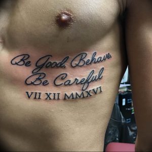 Фото тату на груди мужчины: фраза 'Be Good. Behave. Be Careful' и римские цифры 'VII XII MMXXVI' выполнены черным цветом.