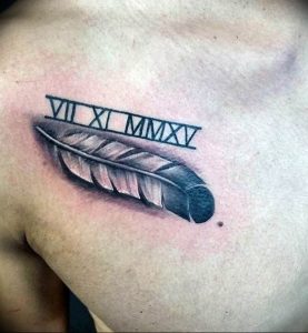 Фото тату: реалистичное изображение пера с римскими цифрами 'VII XI MMXV' над ним на мужской груди. Стильный и символичный дизайн.