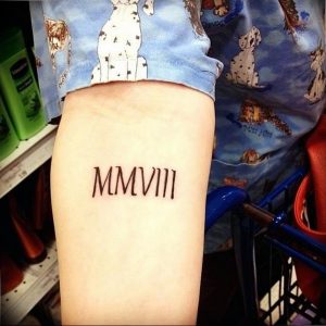 Фото тату: черные римские цифры 'MMXVIII' на внешней стороне бедра. Простой и лаконичный дизайн, популярный выбор для памятных дат.
