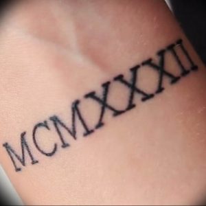 Фото татуировки с римскими цифрами MCMXXII на коже. Черный цвет, четкие линии, минималистичный дизайн.