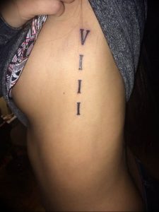 Фото тату: вертикальная цепочка римских цифр 'V I I I' на женском боку, тонкие линии, простой дизайн, рисунок татуировки.
