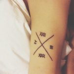 Фото тату: римские цифры 'XXIII' и 'V' пересекаются на предплечье. Минималистичный дизайн, оригинальная композиция.