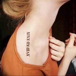 Фото тату: черные римские цифры 'XIX-XII-XXIX' вдоль ключицы женщины. Элегантный минималистичный дизайн, подчеркивающий изящные линии тела.