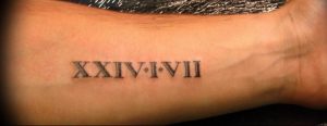 Фото тату: черные римские цифры 'XXIV-I-VII' на запястье мужчины. Простой и лаконичный дизайн, четкие линии.
